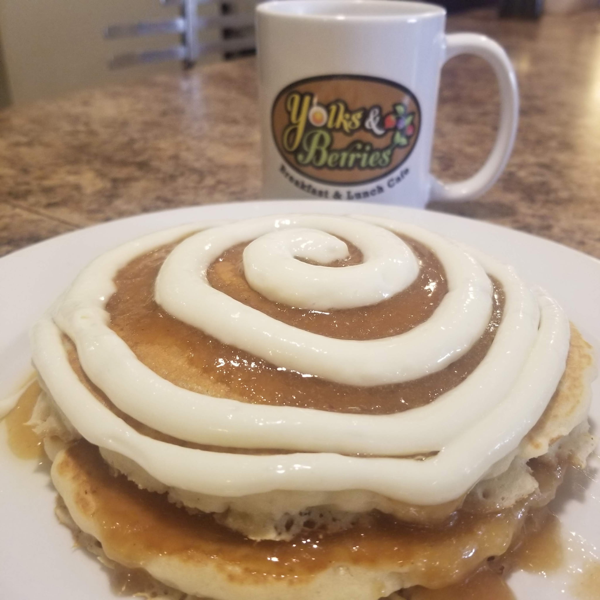 Cinnamon roll pancakes with icing and a Yolks & Berries coffee mug